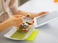 Closeup on young woman eating fruits salad and using tablet pc