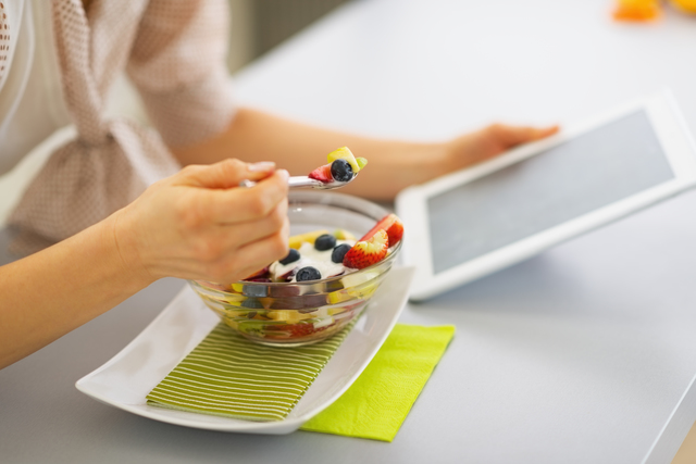 Closeup on young woman eating fruits salad and using tablet pc