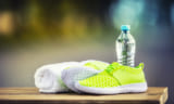 Pair of yellow green sport shoes towel water smart pone and headphones on wooden board. In the background forest or park trail.Accessories for running sport