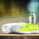 Pair of yellow green sport shoes towel water smart pone and headphones on wooden board. In the background forest or park trail.Accessories for running sport