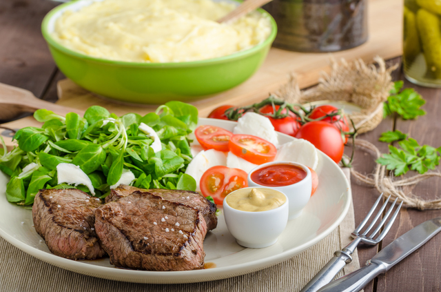 Beef steak with salad, mozzarella and tomatoes, two dip and mashed potato behind