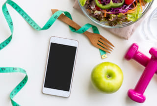 Fresh salad with green apple, dumbbell, measuring tape and empty screen smartphone on white background. Diet, healthy eating concept