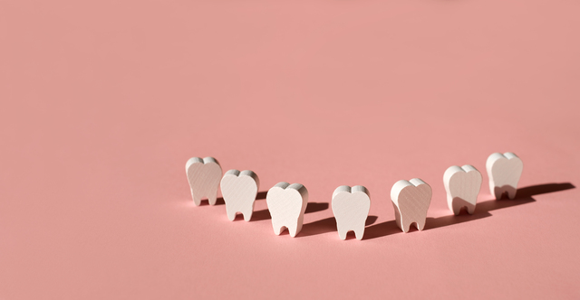 Teeth models standing in a row making a smile on a pink background.