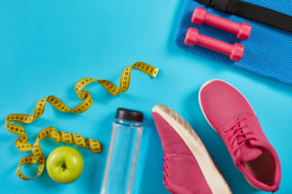 Sneakers with measuring tape on cyan blue background. Centimeter in yellow color, pink sneakers, dumbbells and bottle of water, copy space.
